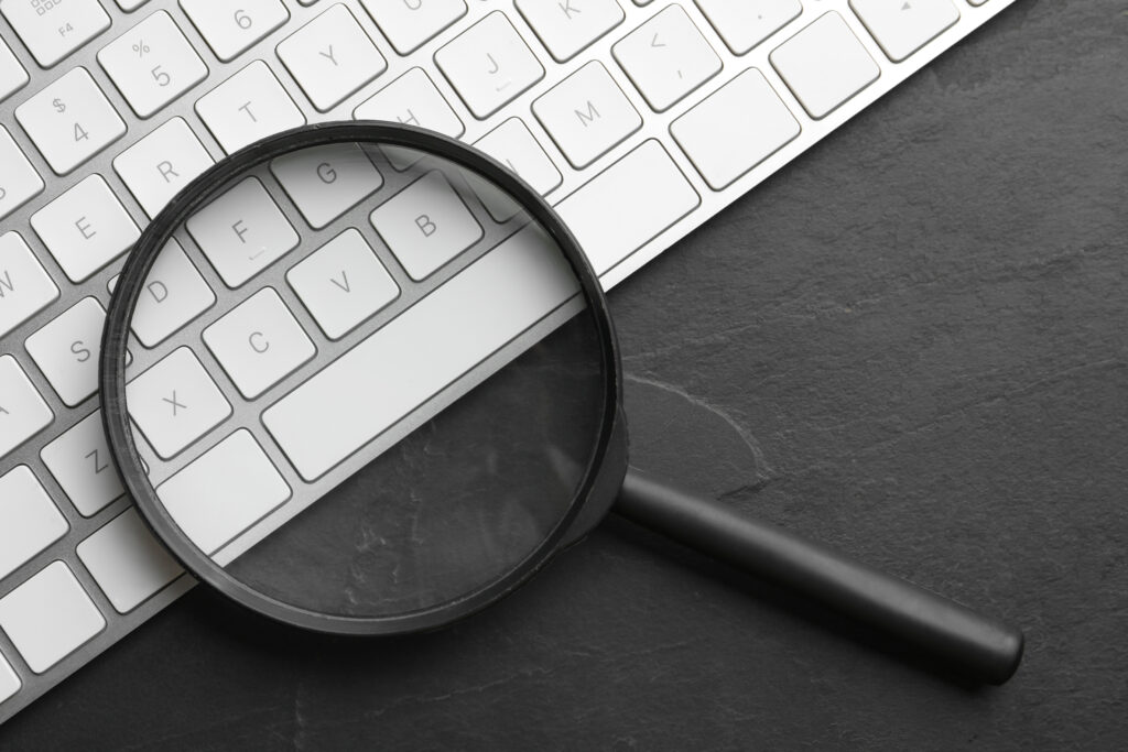 Magnifier Glass And Keyboard On Black Slate Background, Flat Lay